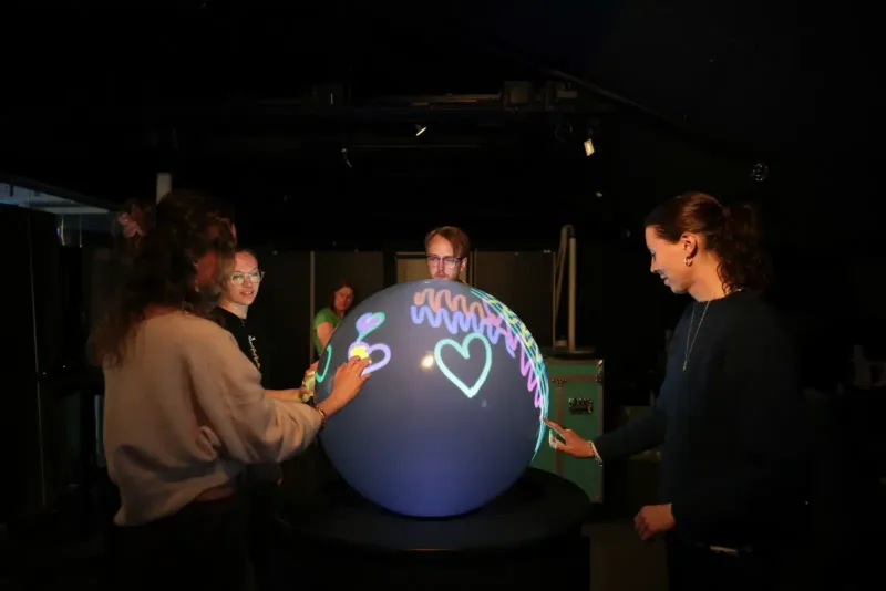 Visitors exploring WISDOME's TellUs experience together on a PufferTouch sphere